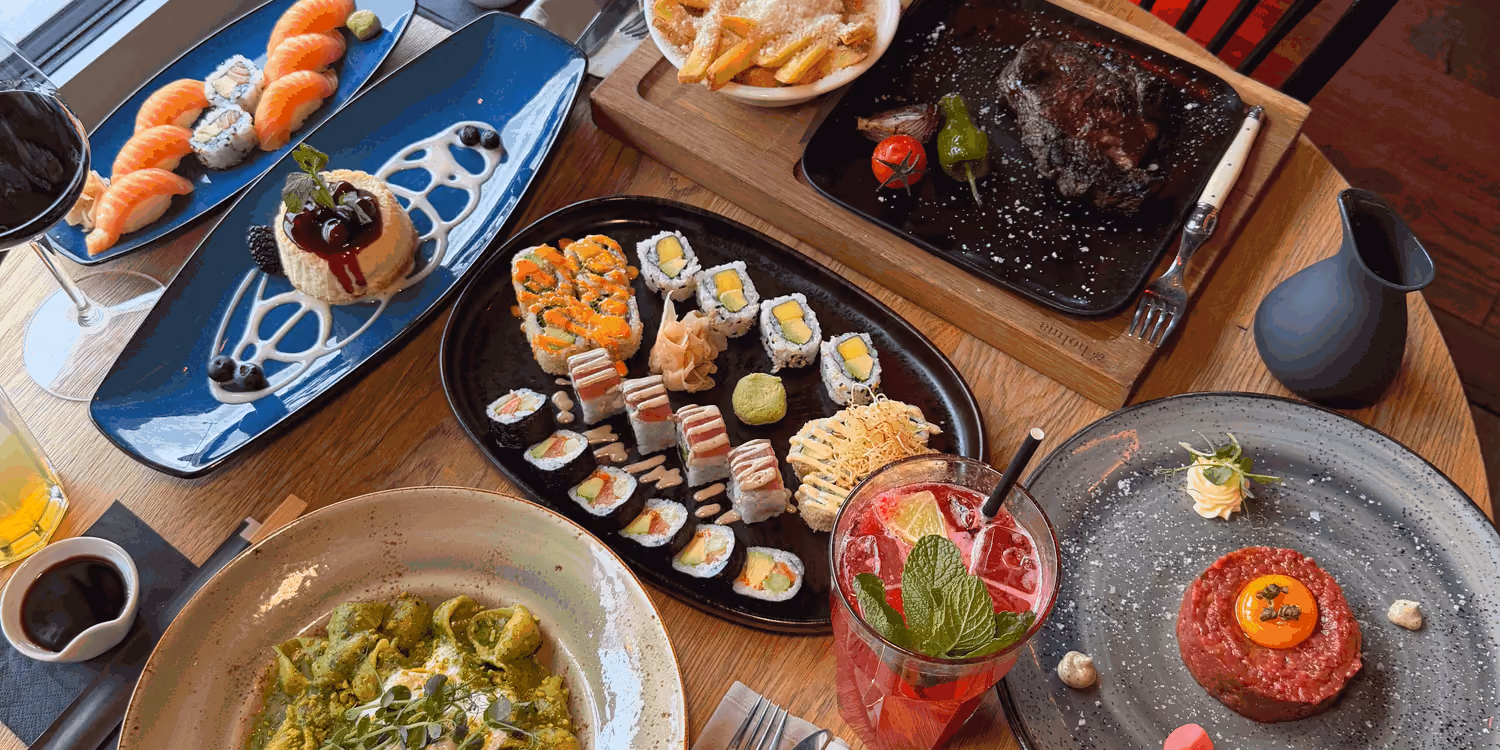 Steak, Sushi, Beef Tatar, Pesto-Pasta und Trüffel-Pommes auf einem runden Holztisch in der Augenweide Wien