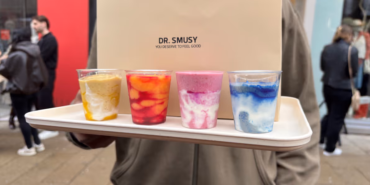 Vier bunte Smoothies auf einem Tablett vor dem Dr.-Smusy-Store in Wien